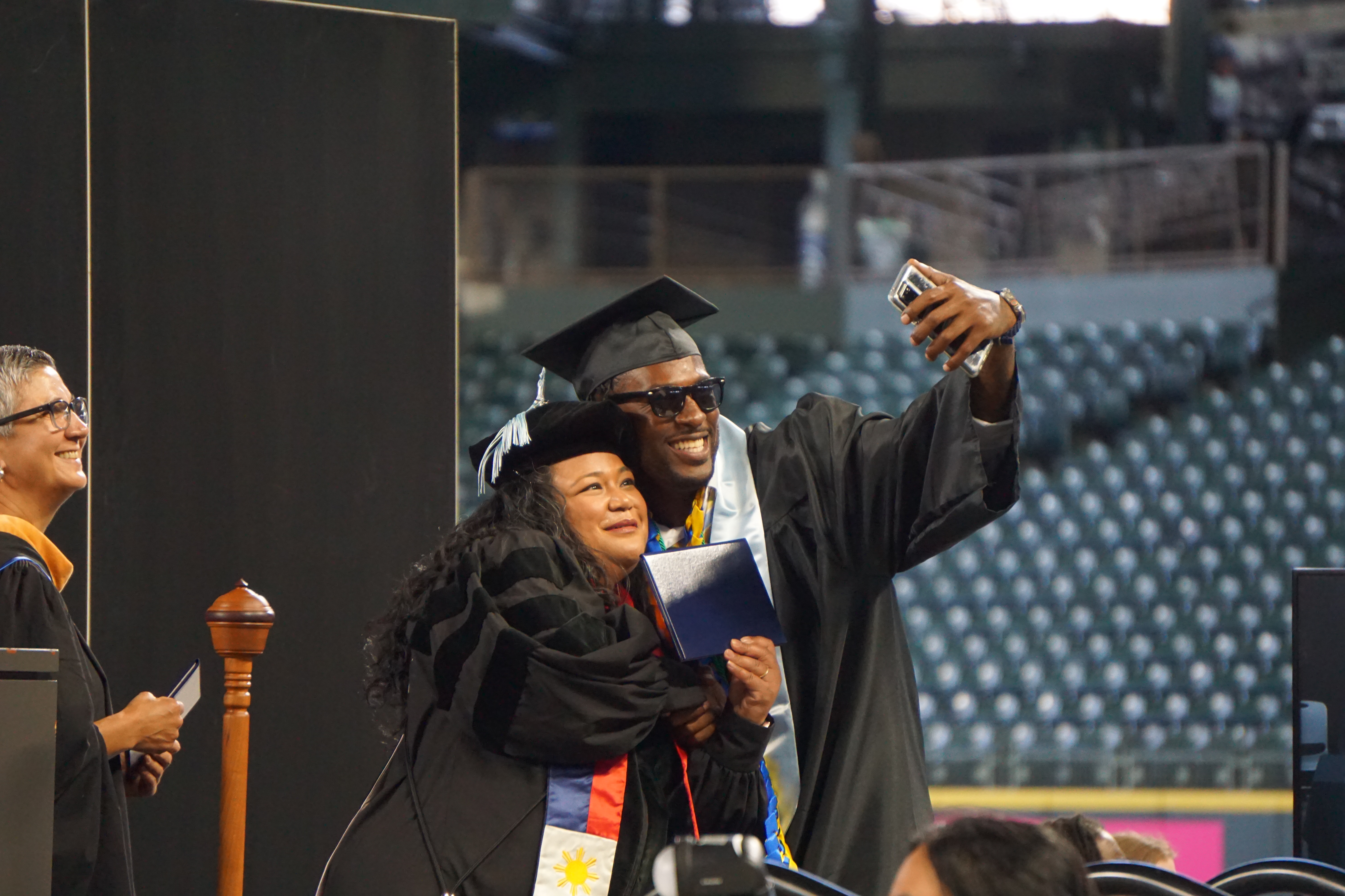 A Bachelor of Applied Science graduate poses for a selfie with Seattle Colleges Interim Chancellor (and former South Seattle College President) Rosie Rimando-Chareunsap as Board of Trustees Vice Chair Rosa Peralta looks on at the Seattle Colleges 2023 Commencement at T-Mobile Park on June 22, 2023. 